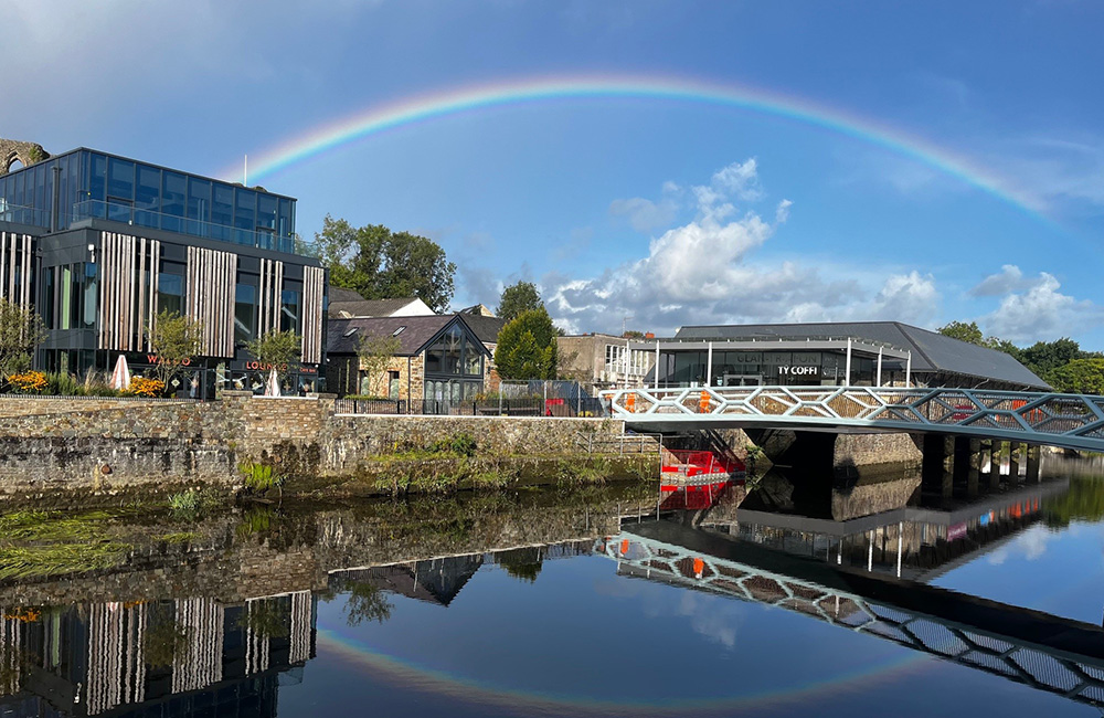 Delwedd o’r bont droed arfaethedig yn Hwlffordd gyda datblygiad Glan Cei'r Gorllewin yn y cefndir